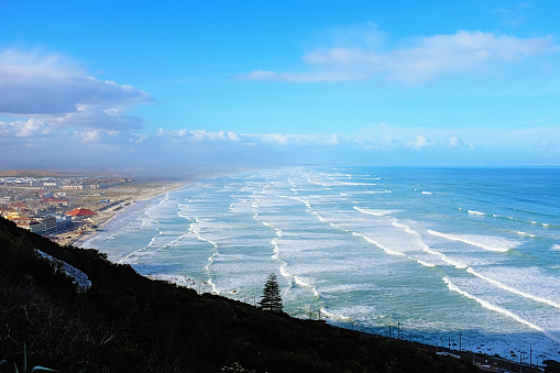 From a hillside, one can see rolling surf and waves heading off as far as the eye can see.