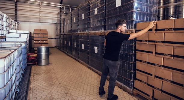 Young businessman looking at the packaged beer boxes in warehouse. Brewery owner verifying the beer boxes in delivery storage area.