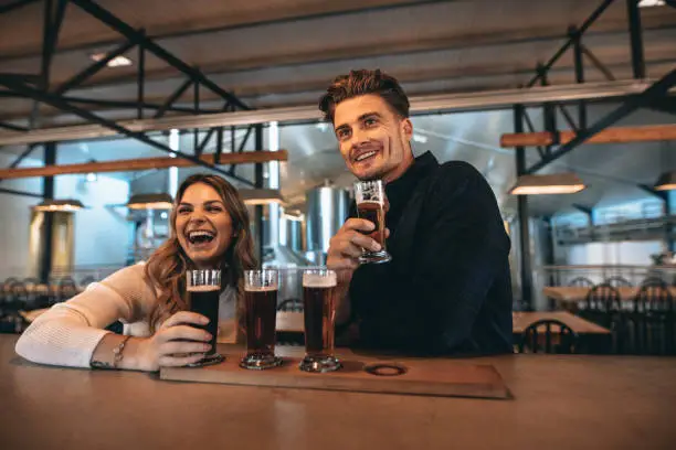 Smiling young couple at the bar with different varieties of craft beers. They are at brewery and tasting beers.