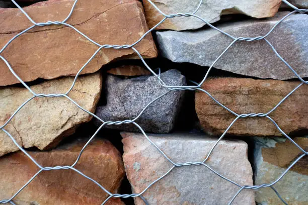 Close up of a gabion retaining-wall system consisting of cut stone enclosed in chicken wire. Construction background.