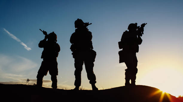 istock Squad of Three Fully Equipped and Armed Soldiers Standing in Desert Environment in Sunset Light. 814366824