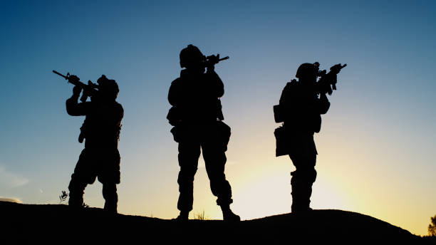 istock Squad of Three Fully Equipped and Armed Soldiers Standing in Desert Environment in Sunset Light. 814366826