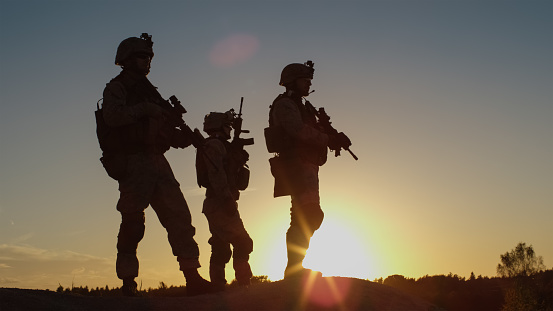 Escuadrón de tres soldados completamente equipados y armados de pie en la colina en medio del desierto en puesta de sol luz. photo