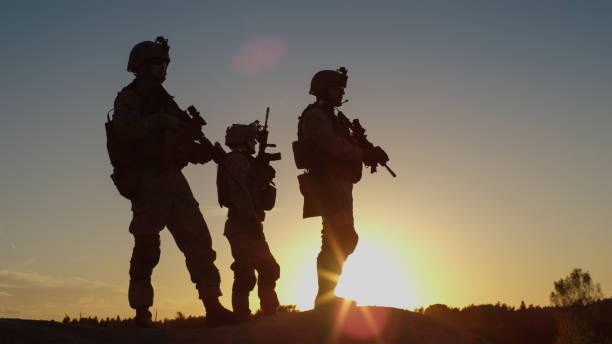 escuadrón de tres soldados completamente equipados y armados de pie en la colina en medio del desierto en puesta de sol luz. - military fotografías e imágenes de stock