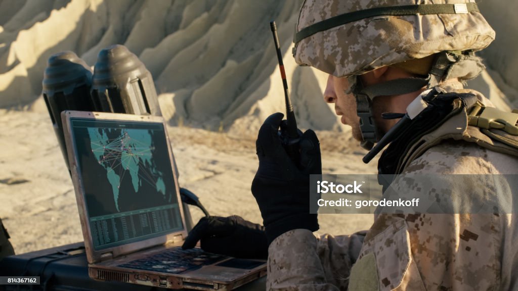 Soldier is Using Laptop Computer and Radio for Communication During Military Operation in the Desert. Military Stock Photo