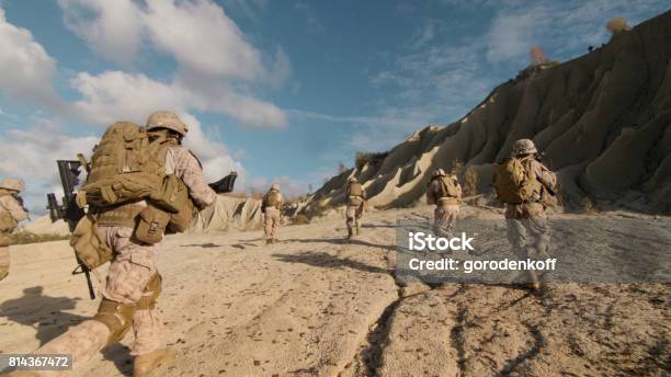Shot Of A Squad Of Soldiers Running Forward And Atacking Enemy During Military Operation In The Desert Stock Photo - Download Image Now