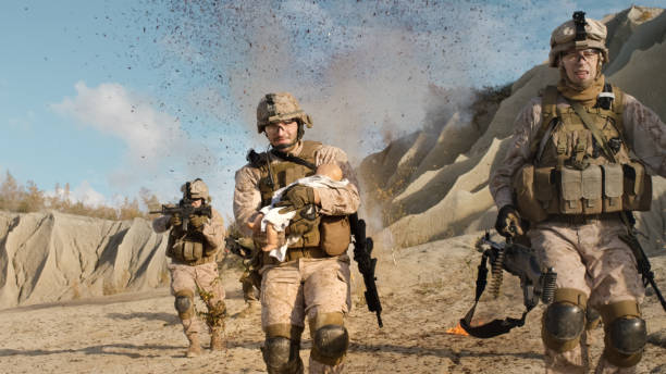 Soldier Running away from Explosions behind Carrying a Baby. While other Members of the Squad Covering Them During Battle in the Desert. Soldier Running away from Explosions behind Carrying a Baby. While other Members of the Squad Covering Them During Battle in the Desert. afghanistan army stock pictures, royalty-free photos & images