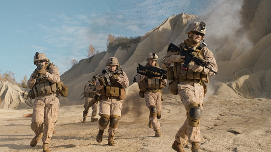 Squad of Fully Equipped, Armed Soldiers Running and Attacking During Military Operation in the Desert.
