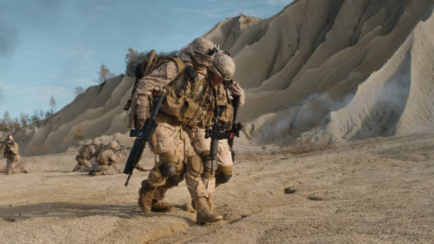 soldado llevando heridos uno mientras que otros miembros del escuadrón cubriendo ellos durante operación militar en el desierto. - iraq conflict fotografías e imágenes de stock