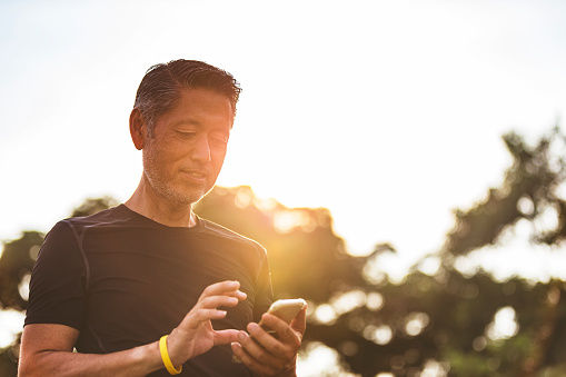 Middle aged Japanese man getting himself ready for an early morning jog, checking his smart technology before he begins