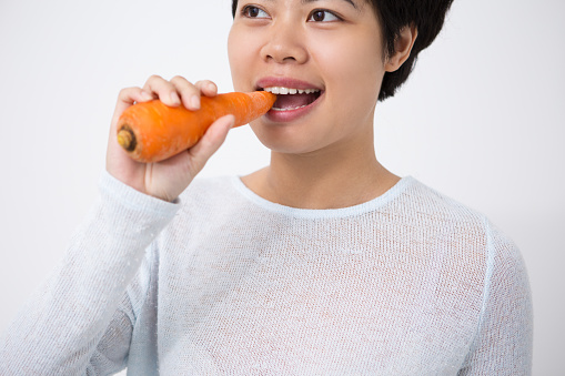 Healthy lifestyle. A woman eating a carrot, detail on the mouth.