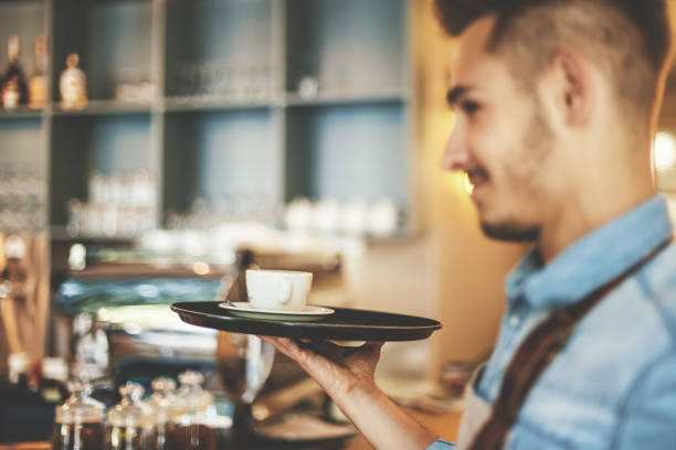 Portrait of happy young waiter with coffee on serving tray.