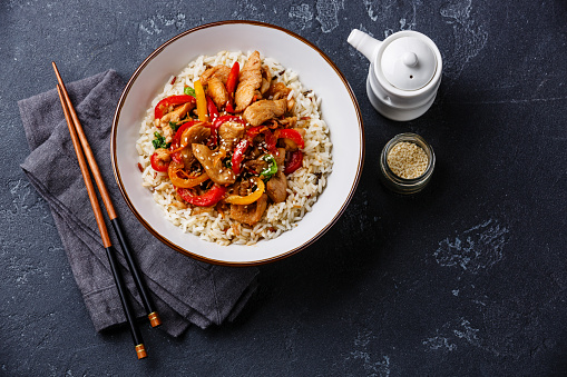 Stir-fry with chicken meat, vegetables and rice in bowl on dark stone background copy space