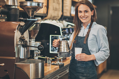 Smiling barista holding a teapot and coffee cup
