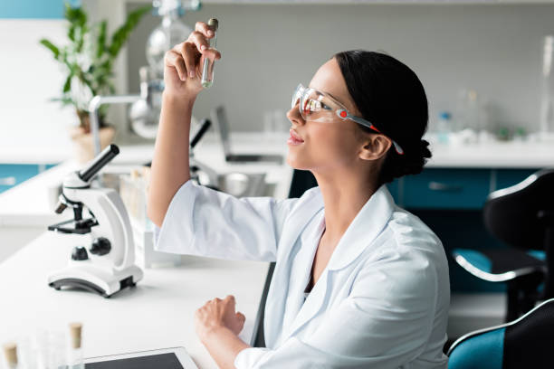 seitliche ansicht der junge chemiker in weiß und schutzbrille mantel prüfung reagenzglas im labor - scientist research test tube lab coat stock-fotos und bilder