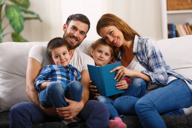 istock Mother and father with children sitting on sofa reading book 814439704