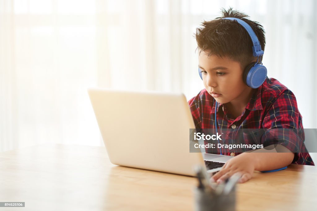 Watching cartoons Cute little boy in headphones watching something on laptop at home Child Stock Photo
