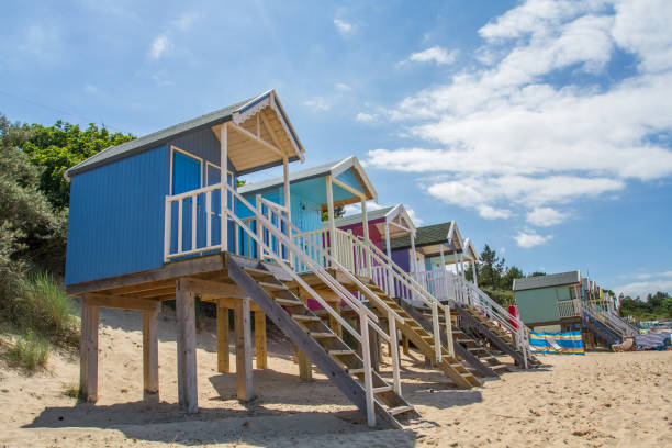 Rows of colourful, wooden beach huts that are elevated on stilts on the white sandy beach of Wells Next The Sea in Norfolk, UK which is a popular tourist destination and travel hot spot.