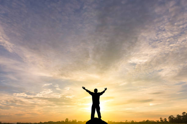 Silhouette of man raised hands at sunset