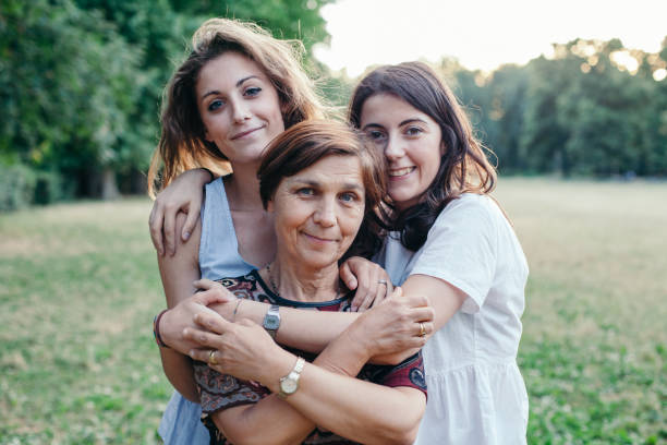 mère et filles embrassent dans un parc au coucher du soleil sur un soir d’été - family with two children family park child photos et images de collection