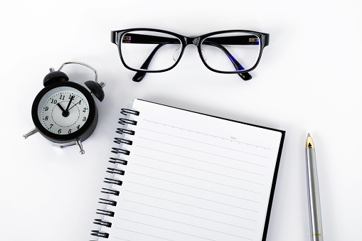 Blank notepad with eyeglasses, pen and alarm clock on white background with film effect.