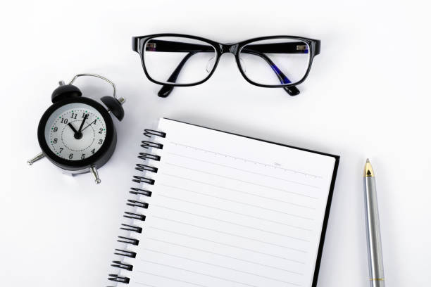 Top view of notepad, eyeglasses, pen and alarm clock Blank notepad with eyeglasses, pen and alarm clock on white background with film effect. black coffee swirl stock pictures, royalty-free photos & images
