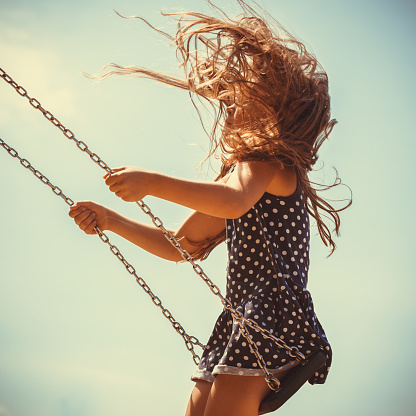 Craziness and freedom. Young summer girl playing on swing-set outdoor. Crazy playful child swinging very high to touch the sky.