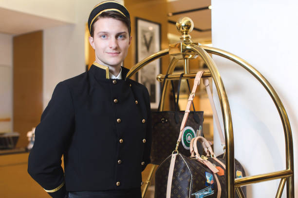 Young man in uniform serving in hotel Smiling man in bellboy uniform standing with luggage cart and looking at the camera bellhop stock pictures, royalty-free photos & images