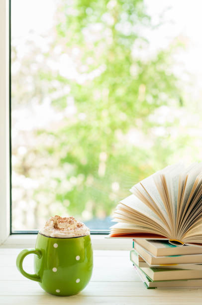 istock Coffee cup with cream and marshmallows, open book on window with bokeh. Reading and breakfast. Concept cozy home 814604992