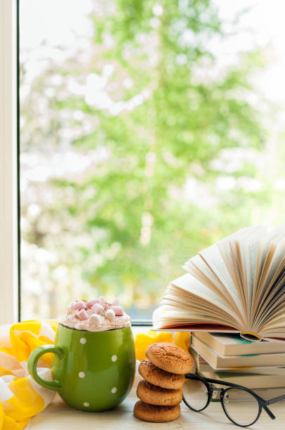 istock Coffee cup, open book, glasses, cookies on window with bokeh. Reading and breakfast. Concept warm and cozy home 814604998