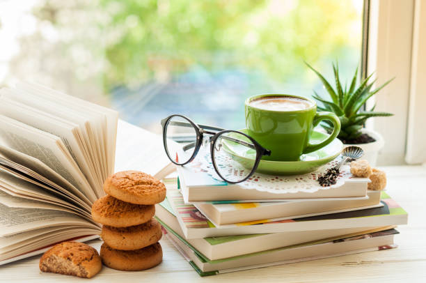 istock Coffee cup, open book, glasses, cookies and flower on window with bokeh. Reading and breakfast. Concept warm and cozy home decor 814605082