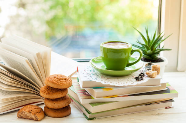 istock Coffee cup, open book, cookies and flower on window with bokeh. Reading and breakfast. Concept warm and cozy home decor 814605140