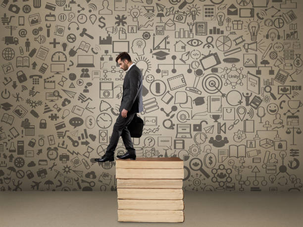 Businessman moving down stack of books in front of icons on wall