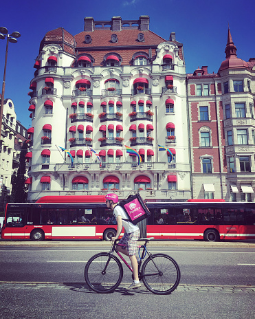 Stockholm, Sweden - August 1, 2016: Foodora  Food Delivery guy on bicycle and bus on Stockholm street.