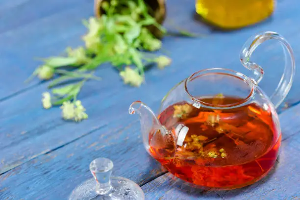 Limeflower tea in glass teapot and lime flowers over blue wood table. Close-up