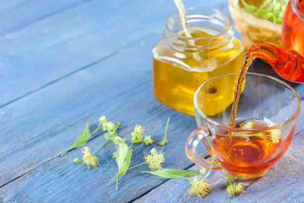 Limeflower tea in glass tea cup, honey and lime flowers over blue wood table. Close-up