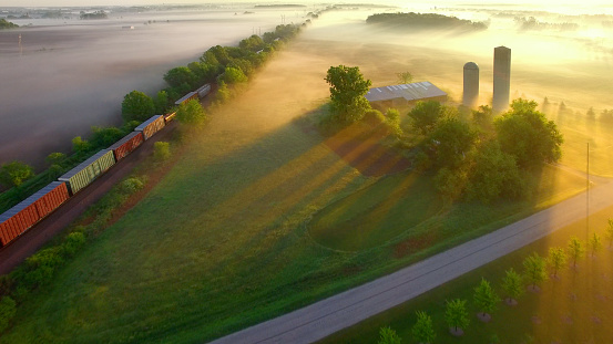 Train rolls through foggy rural landscape at dawn.