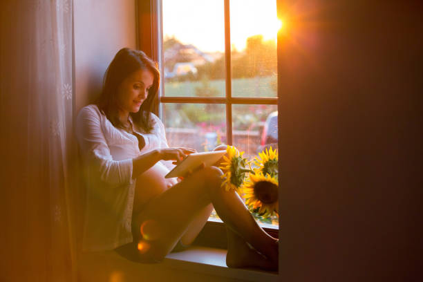 Beautiful pregnant woman, sitting on window shield, reading from tablet