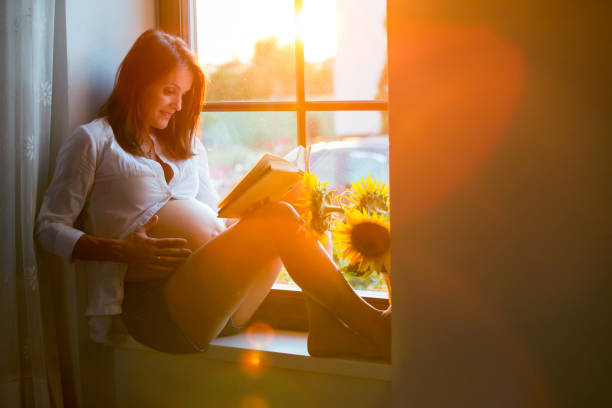 istock Beautiful pregnant woman, sitting on window shield, reading a book 814660542