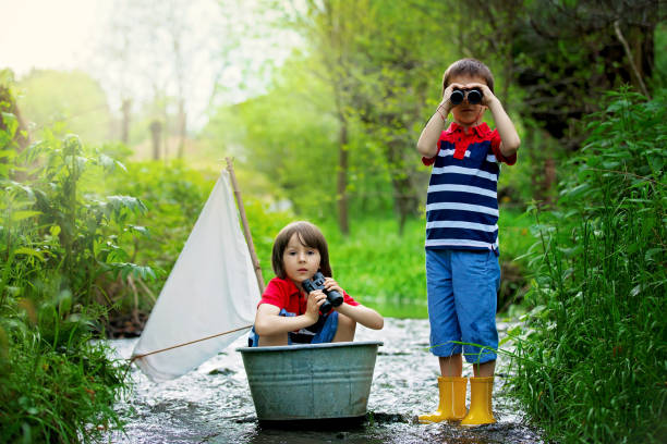 cute children, boys, playing with boat on a little river - children only tree area exploration freshness imagens e fotografias de stock