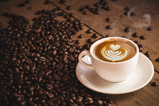 Granos de café y taza de café caliente con arte del latte sobre fondo de madera. vista lateral con espacio de copia de su texto photo