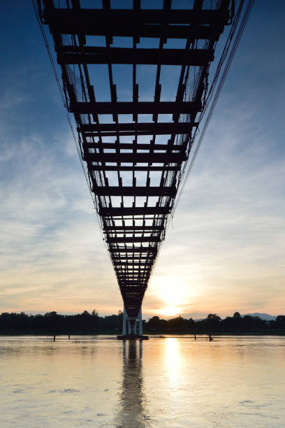 istock Old suspension footbridge across river with sunset. 814801828