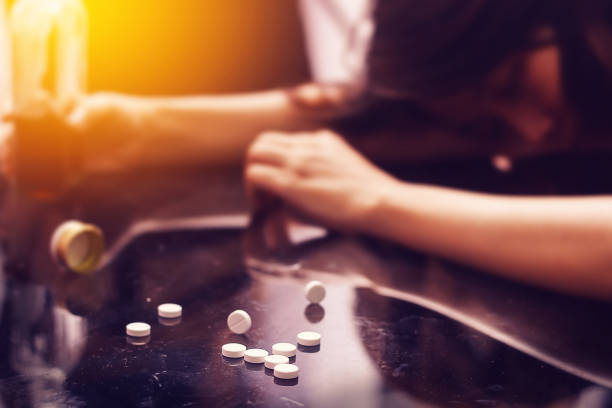 overdose, concetto di problema di tossicodipendenza: diverse pillole versate sul tavolo vicino bottiglia di alcol. - alcohol drug abuse alcoholism pill foto e immagini stock