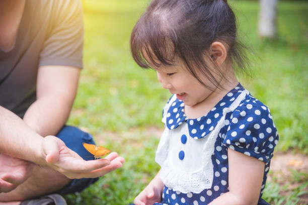 girl looking at butterfly on father hand in park stock photo