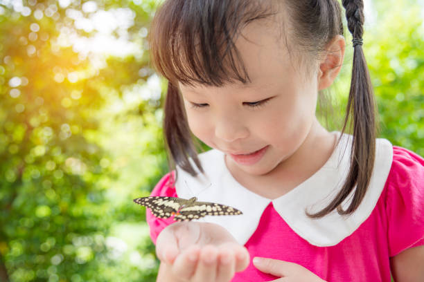 istock girl looking at butterfly on her hand in park 814893968