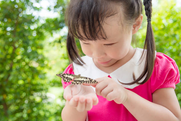 istock girl looking at butterfly on her hand in park 814893976