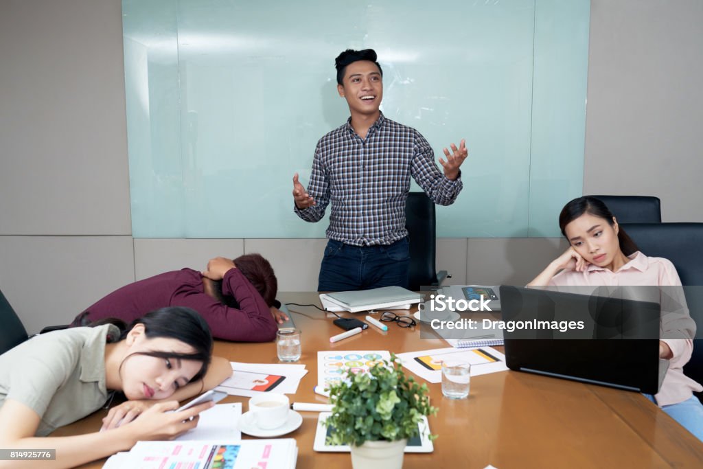 Full of enthusiasm Enthusiastic Vietnamese businessman telling his idea to bored coworkers Boredom Stock Photo