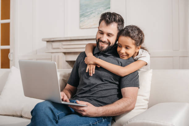 istock multicultural father with daughter sitting on sofa and using laptop at home 814956980