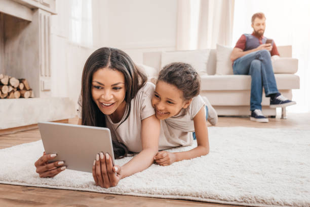 istock Smiling african american mother and daughter using digital tablet while lying on carpet at home 814959978