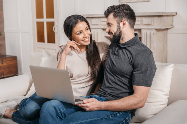 istock smiling multicultural couple sitting on sofa at home with laptop on knees 814962368